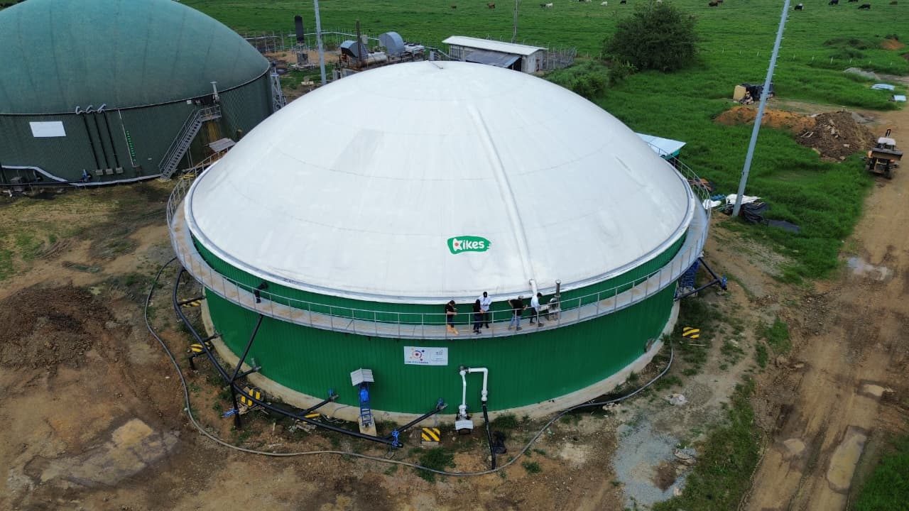 Vista aérea de biodigestor com cúpula branca e tanque verde, com equipe sobre a passarela